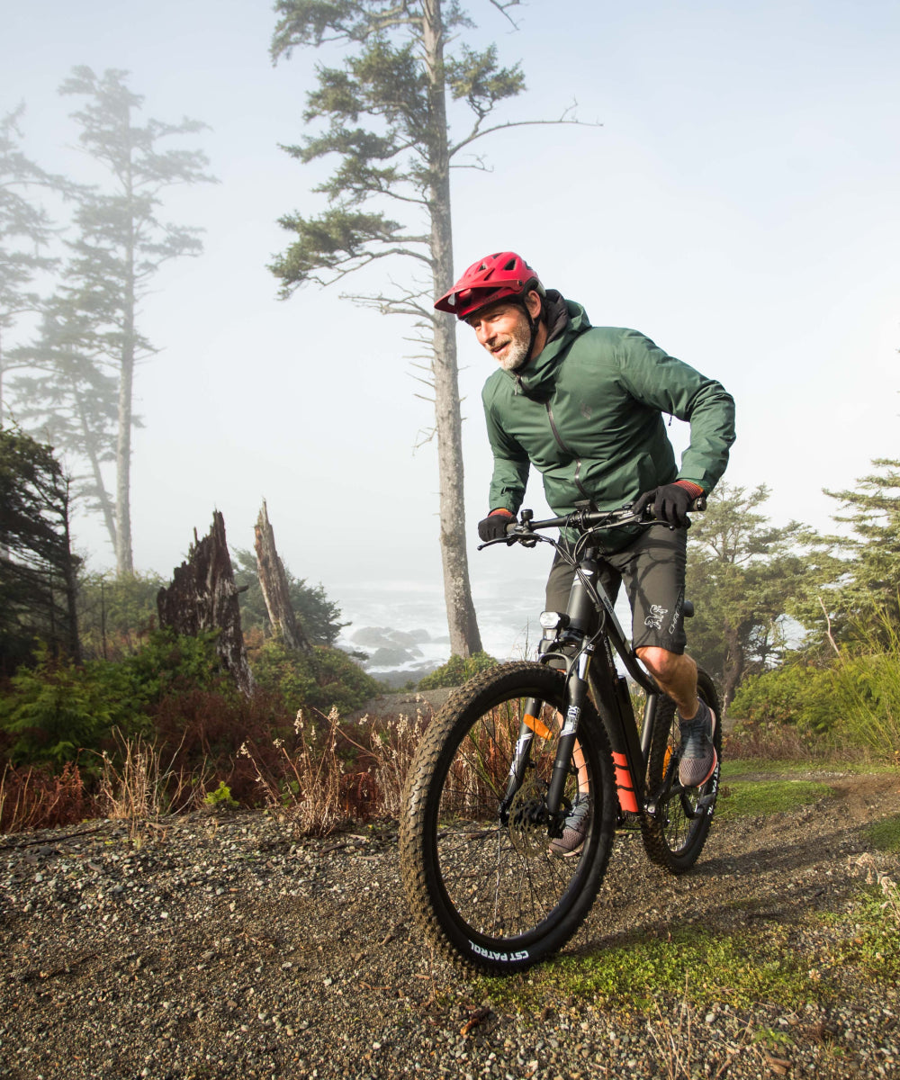 older bearded man with a red helmet riding an electric mountain bike by the coast